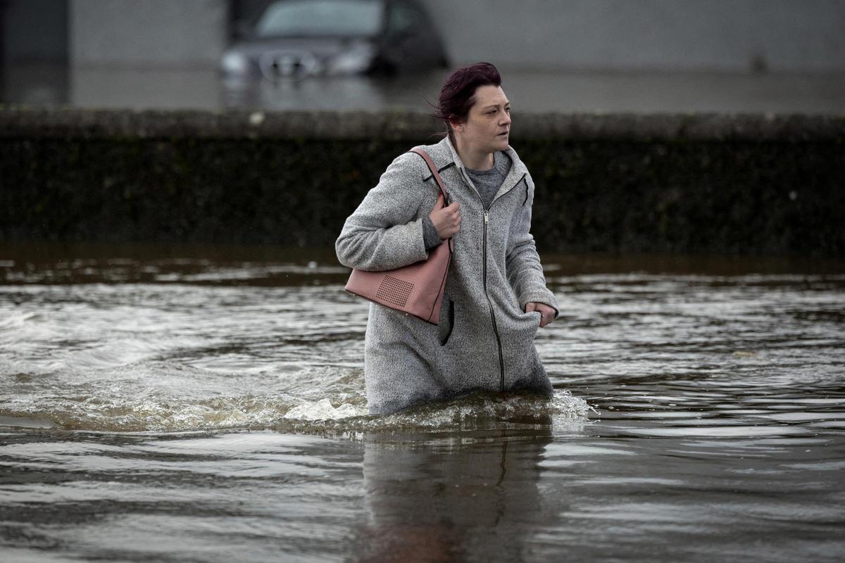 Una mujer intenta caminar sobre el agua que fluye por las calles después de que las fuertes lluvias provocaron grandes inundaciones, antes de la llegada de la tormenta Ciaran, en el centro de la ciudad de Newry, Irlanda del Norte, el 31 de octubre de 2023.