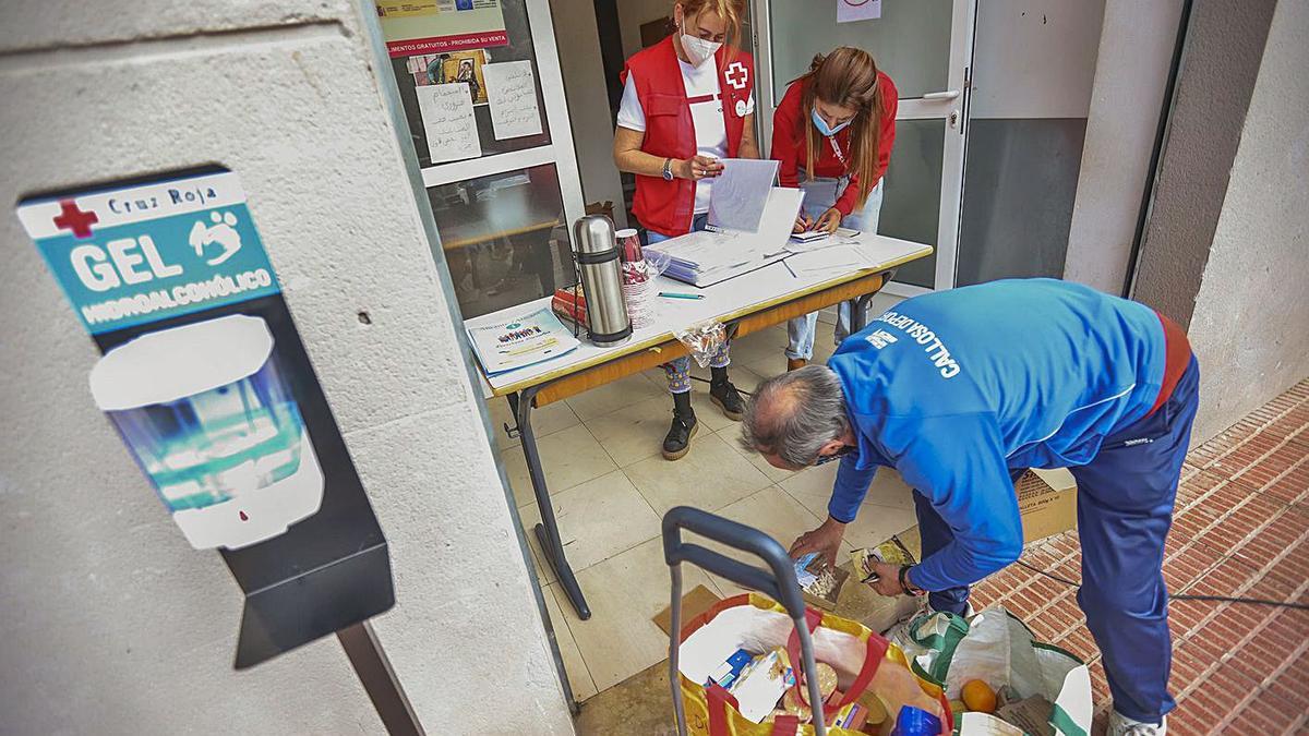 Personal de Cruz Roja entrega alimentos y una bolsa de mascarillas a una persona sin hogar. | TONY SEVILLA