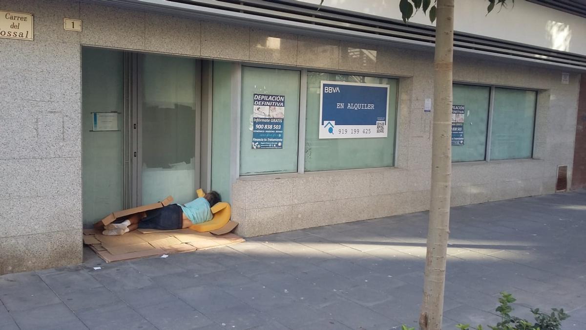 Un hombre duerme a la puerta de un antiguo banco en Gandia