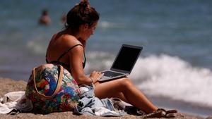 Una mujer toma el Sol mientras mira su ordenador portátil