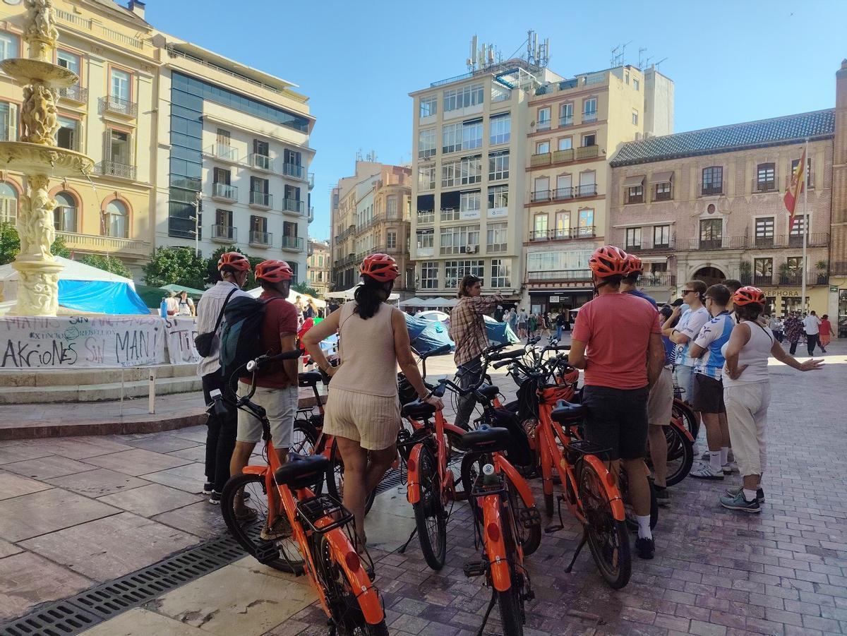 La acampada en la Plaza de la Constitución continúa, mientras un guía turístico acompañada a unos turistas.