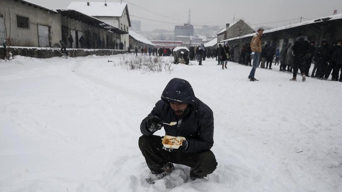 Un refugiado come en medio de la nieve en Belgrado.