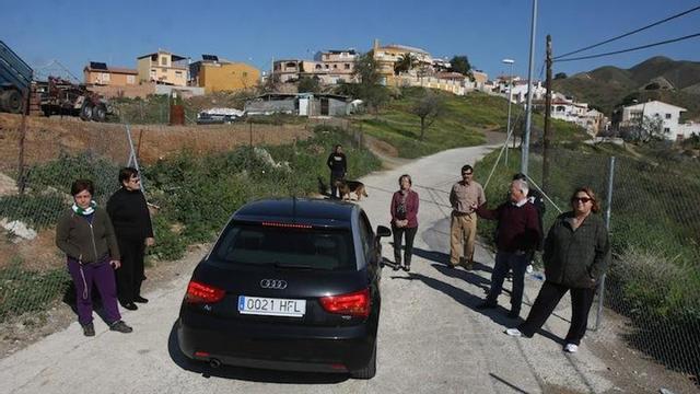 Grupo de vecinos en el Camino de Orozco con El Chaparral al fondo, una carretera sin aceras ni asfaltado en condiciones.