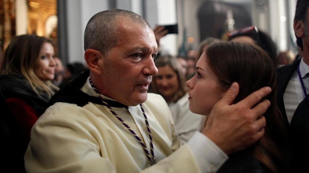 Antonio Banderas abraza a su hija, Estela del Carmen, antes de salir como penitente de Las Lágrimas. A la izquierda, la novia del actor.