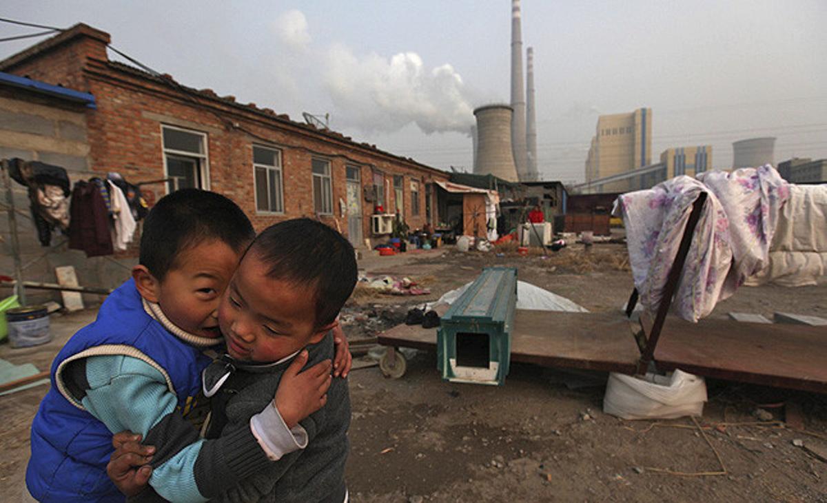 Dos nens juguen al pati de casa al costat d’una planta energètica a Pequín, Xina.