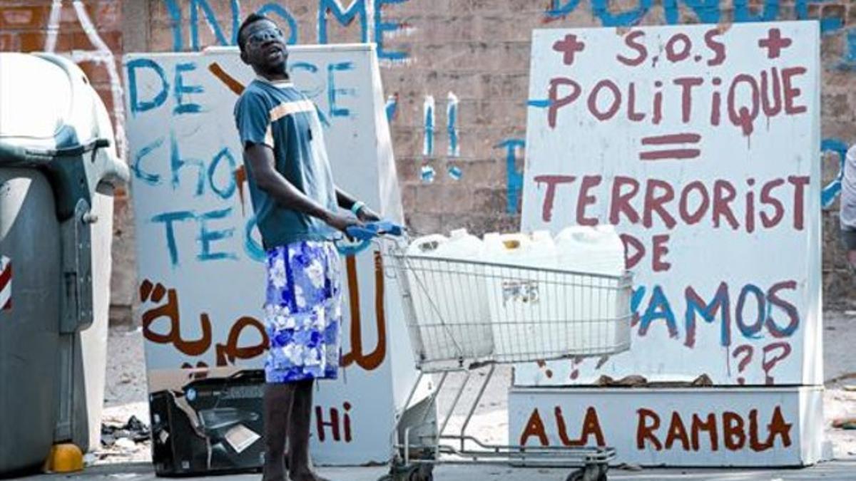 Un joven africano transporta agua en un carrito de supermercado ante pintadas reivindicativas de los ocupantes de la antigua fábrica de Sant Marí, ayer.