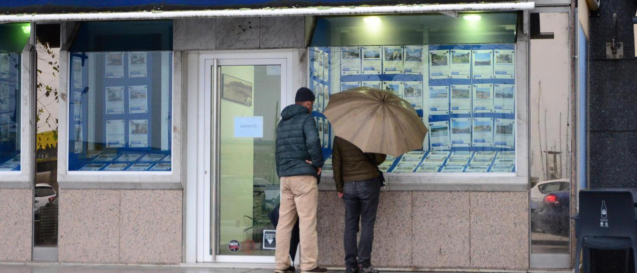 Dos personas observan ayer los carteles en el escaparate de una inmobilaria en el centro de Cangas.