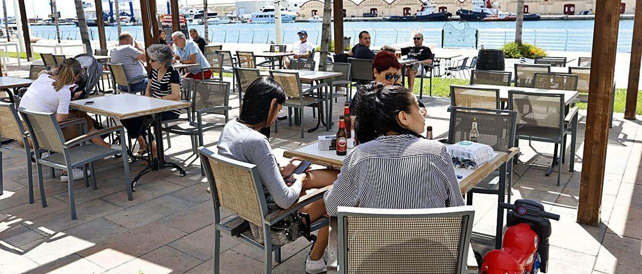 Clientes en una terraza en la playa, en la bocana del puerto frente a los tinglados.