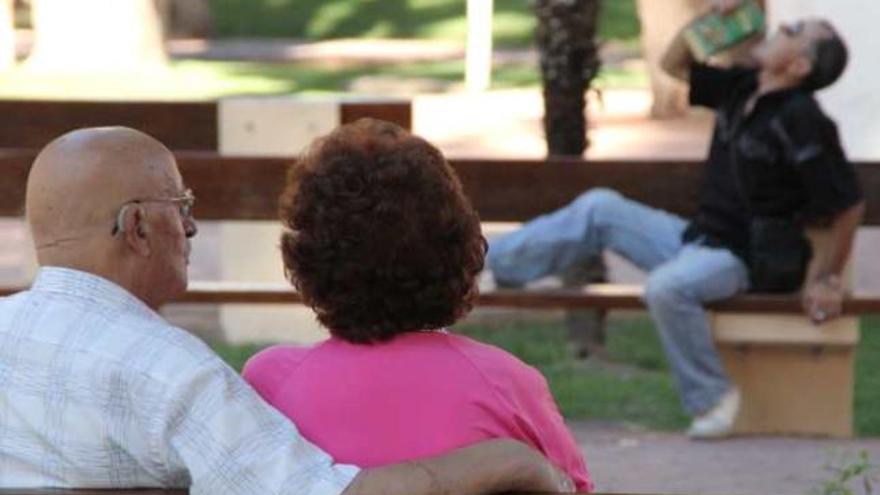 Una pareja de mayores observa en un parque de Elda a un hombre consumiendo vino.