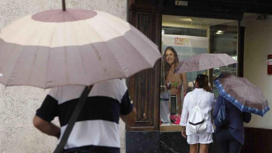 Viandantes resguardándose de la lluvia con paraguas en la calle San Lorenzo.