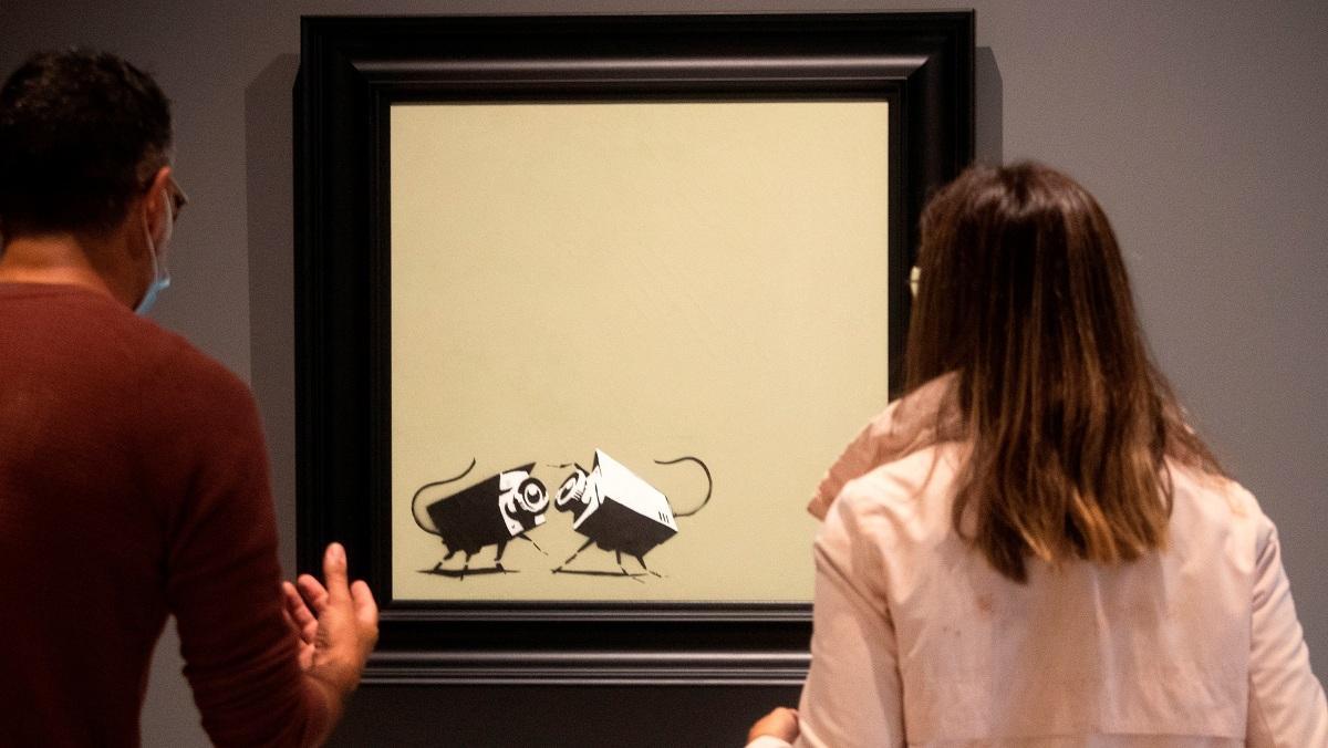 Una pareja contempla las dos cámaras de CCTV, obra creada por Banksy.