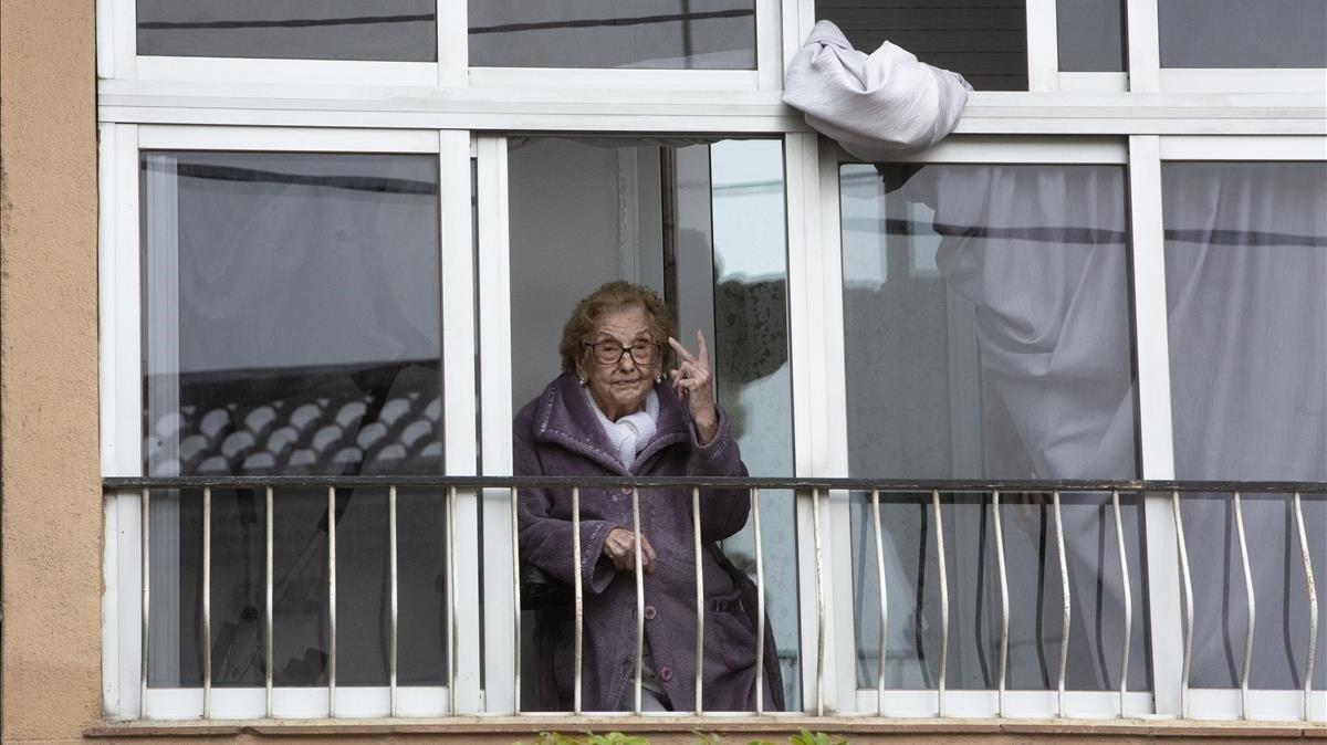 Otilia Augusta saluda con el signo de victoria desde su domicilio en el barrio de Singuerlín en Santa Coloma de Gramenet.