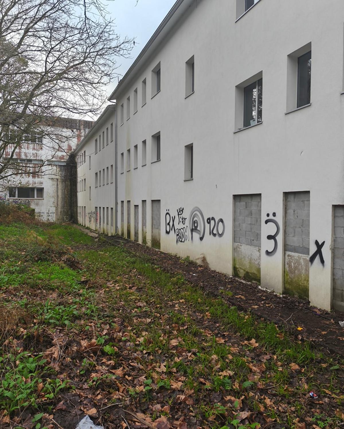 Pintadas y humedades en los edificios de las viviendas de alquiler social de Rianxo, en cuyo entorno hay además acumulación de barro y maleza.