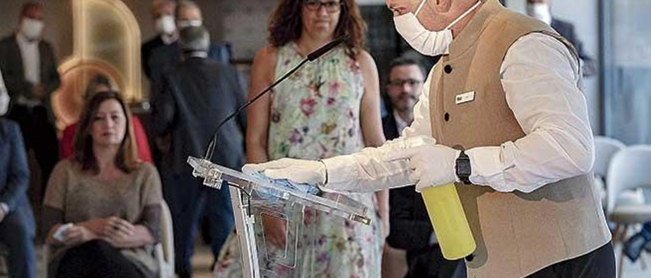 Un trabajador de Riu desinfecta el atril de los oradores ante la atenta mirada de las autoridades.