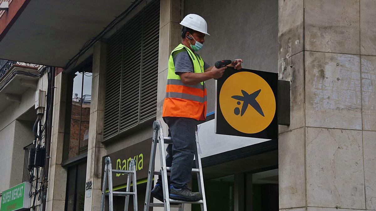 Un operari col·locant el logotip de CaixaBank en una oficina de Bankia.  | ACN