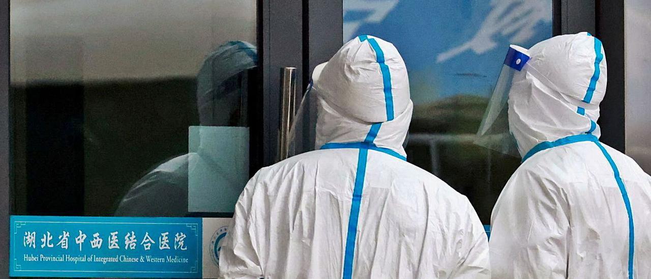 Dos trabajadores en la puerta de un hospital de Wuhan durante la investigación de la OMS.   | // T. PETER