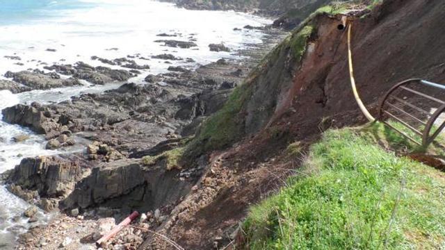 el saneamiento, en el aire. El desprendimiento ocurrido en la senda costera del Tranqueru rompió el conducto de saneamiento (de color rojo) que aparece tirado en el pedrero. Como solución de emergencia, el concejo echará mano de los dos aliviaderos de la zona, uno en Perán y el otro en Candás.