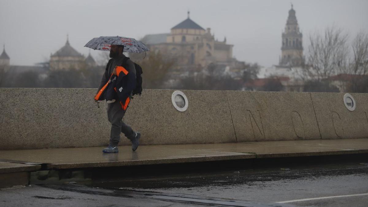 Un hombre se protege de la lluvia con un paraguas con la Mezquita-catedral al fondo.