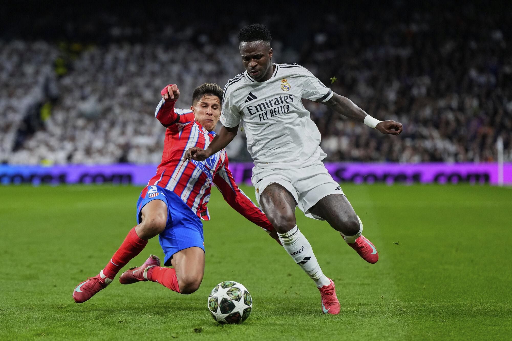Atletico Madrid's Giuliano Simeone, left, fights for the ball with Real Madrid's Vinicius Junior during the Champions League round of 16 first leg soccer match between Real Madrid and Atletico Madrid at the Bernebeu stadium in Madrid, Spain, Tuesday, March 4, 2025. (AP Photo/Manu Fernandez)