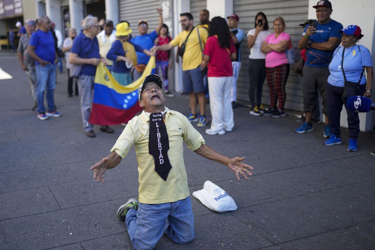 A man wearing the phrase in Spanish Fight for freedom kneels during a demonstration by opponents of Venezuelan President Nicolas Maduro the day before his inauguration for a third term in Caracas, Venezuela, Thursday, Jan. 9, 2025. (AP Photo/Matias Delacroix). EDITORIAL USE ONLY / ONLY ITALY AND SPAIN