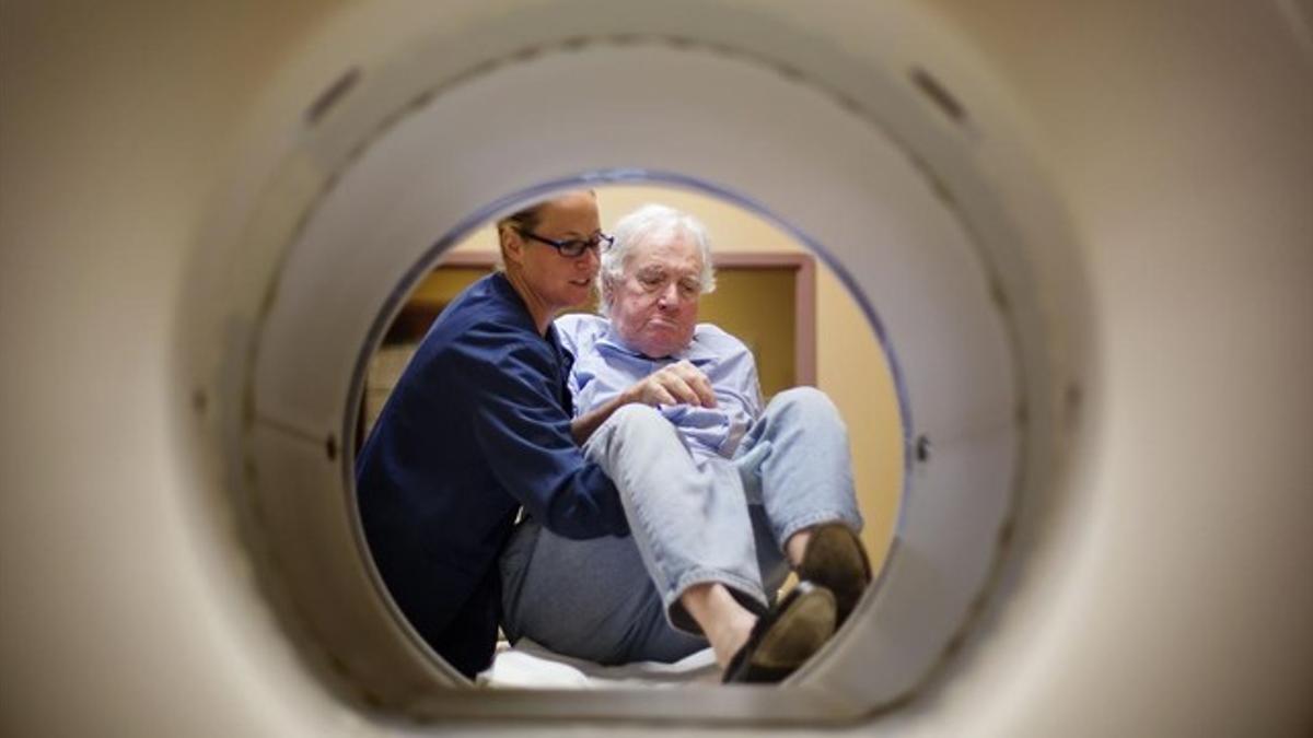 Una enfermera prepara a una paciente para someterse a una tomografía para conocer la evolución de su cáncer