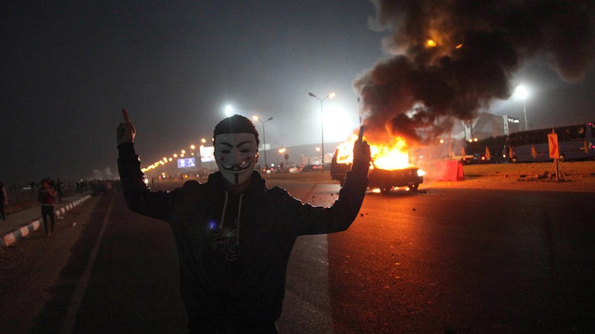 Un aficionado con máscara, junto a un coche en llamas en el exterior del estadio de la Defensa Aérea, en el este de El Cairo