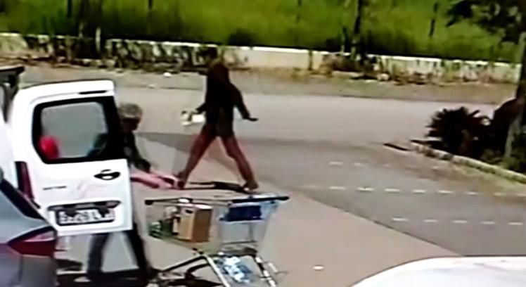 Uno de los ladrones se acerca a un coche para robar mientras las víctimas cargan la compra.
