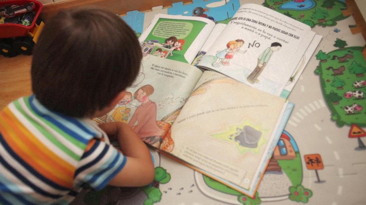 Un niño de tres años mira las viñetas de los cuentos infantiles sobre el abuso sexual '¿De qué color son tus secretos?', 'No te calles' y 'Tu cuerpo es tu tesoro'
