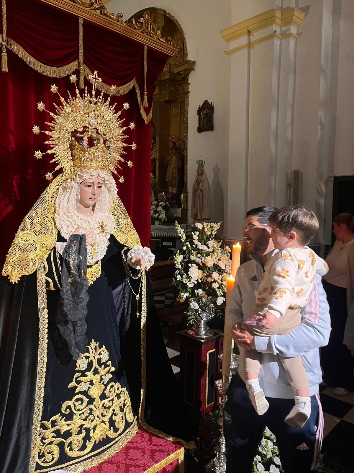 Un padre se acerca con su hijo a la Virgen de los Dolores de El Carpio, expuesta en besamanos.