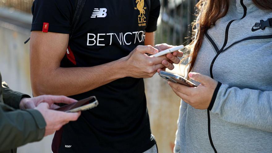 Varios jóvenes usan su teléfono móvil a la salida de la jornada escolar. | TONI ESCOBAR