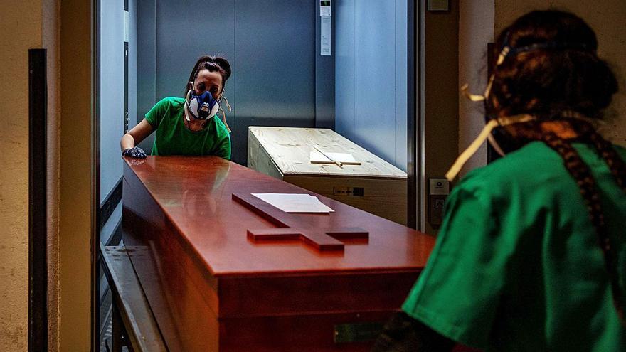 Dos operarias trasladan los restos mortales de una víctima de la Covid. | ENRIC FONTCUBERTA