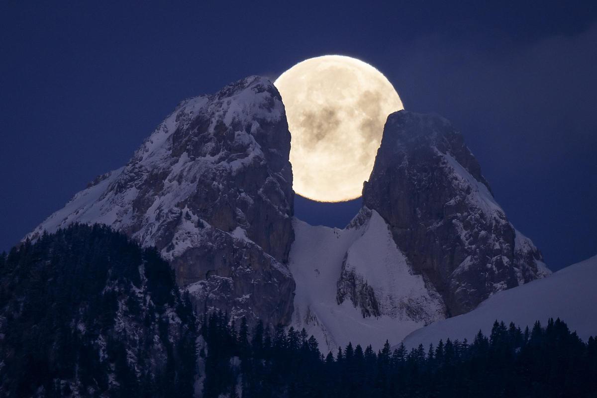 Vista de la luna llena desde Aigle (Suiza), ocultándose tras los picos gemelos de Les Jumelles, en el Chablais Valaisan, en febrero de 2023.