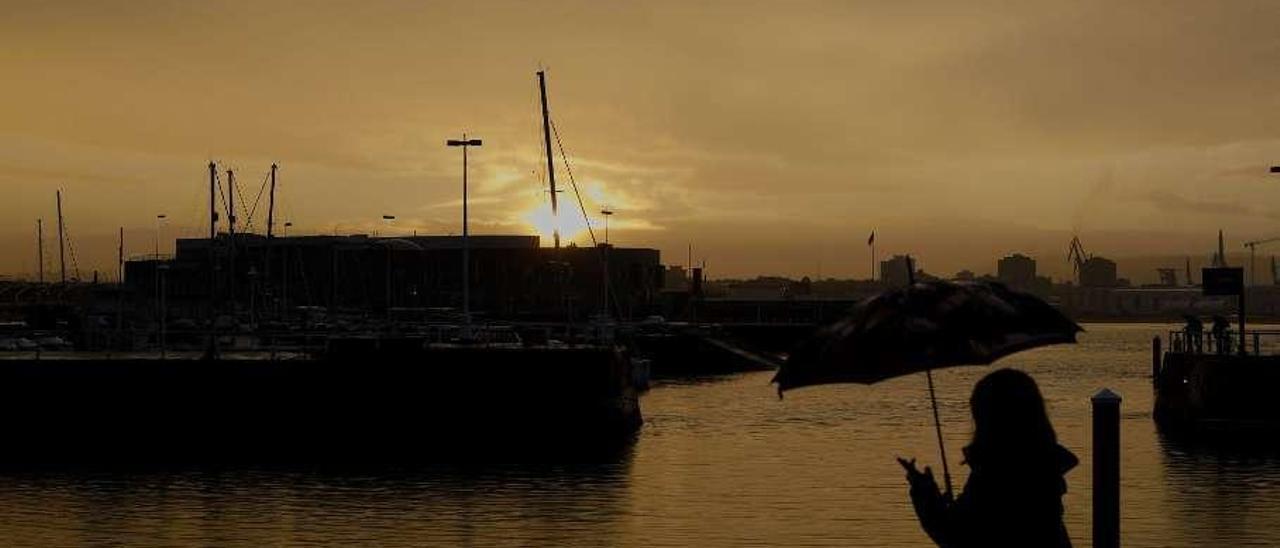 Una mujer pasea frente al puerto deportivo con el móvil en la mano.