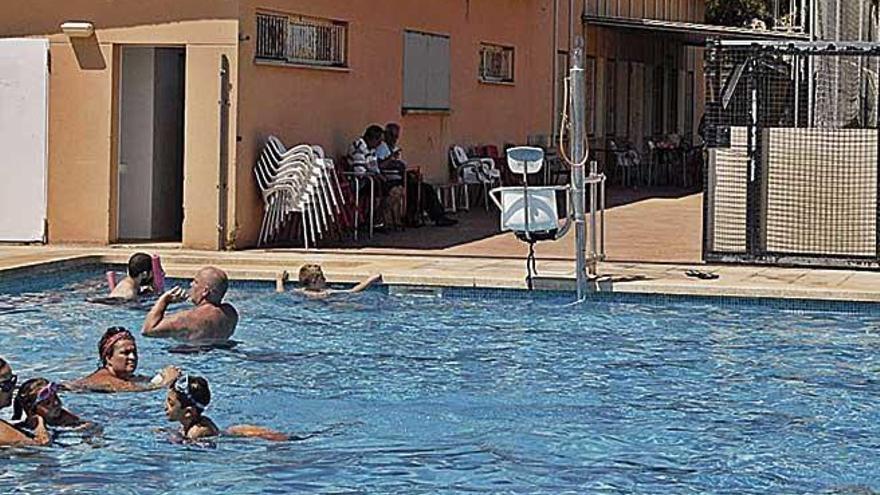 Usuarios de la piscina de Pòrtol bañándose ante el bar cerrado.