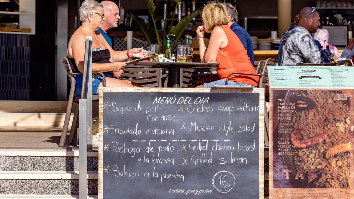Unos turistas comen detrás de un cartel de menú del día en la zona inglesa de Benidorm.