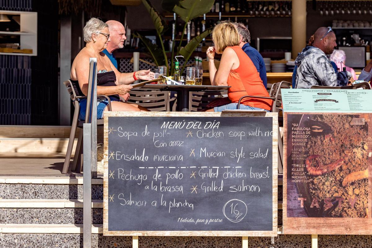 Unos turistas comen detrás de un cartel de menú del día en la zona inglesa de Benidorm.