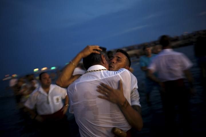 Men in traditional costumes embrace after carrying a statue of the El Carmen Virgin into the sea during a procession in Malaga