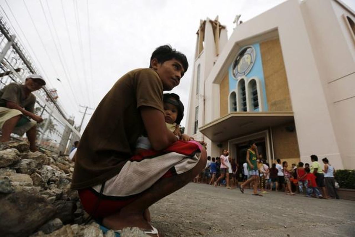 Diversos filipins descansen davant una església convertida en centre d’evacuació de cara a l’impacte del supertifó Hagupit sobre la ciutat de Tacloban (Filipines).