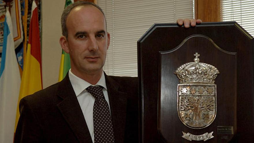 El alcalde de Curtis, Javier Caínzos, con el escudo del municipio.