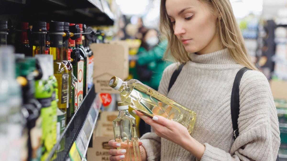Una mujer leyendo la etiqueta de una botella de aceita de oliva