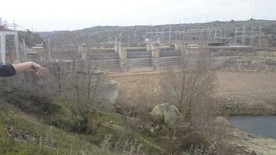 Una persona muestra el bajo nivel del embalse de Ricobayo, con el agua lejos del gran aliviadero.