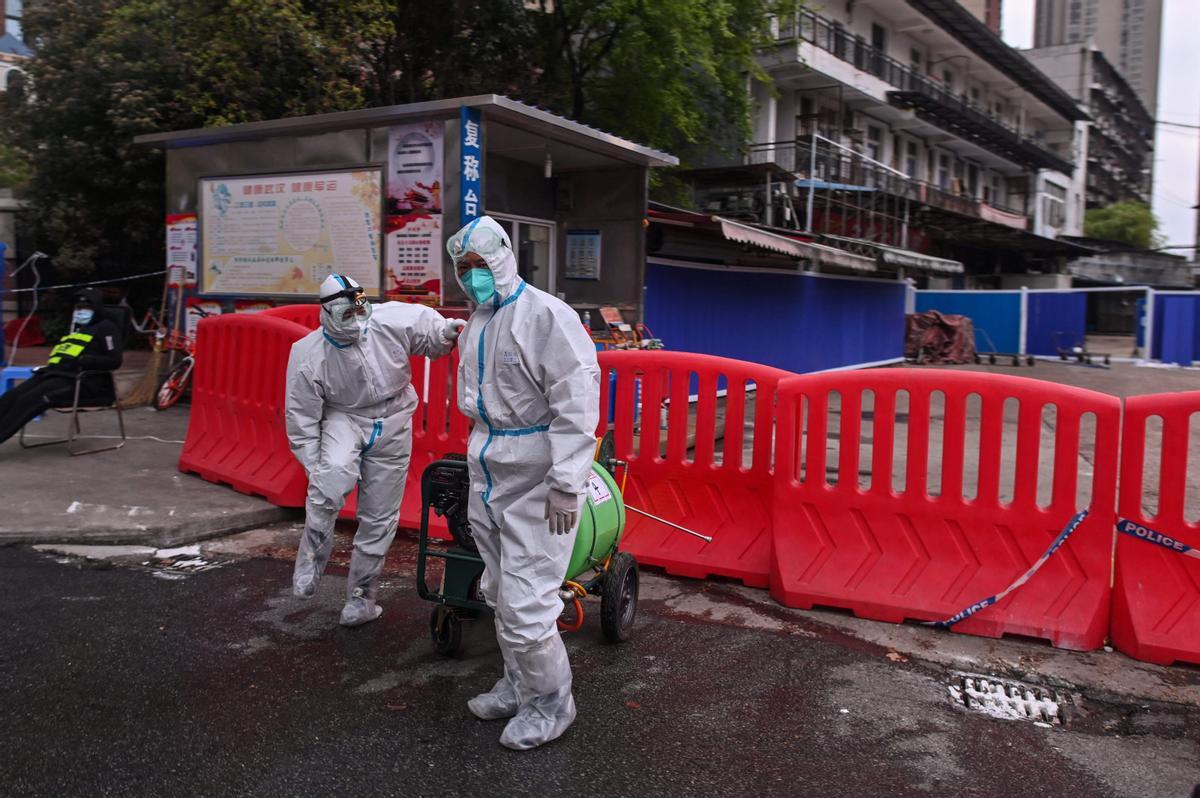 Unos trabajadores con traje de protección caminan junto al mercado mayorista de marisco de Huanan, en Wuhan, en la provincia central china de Hubei. Unos trabajadores con traje de protección caminan junto al mercado mayorista de marisco de Huanan, en Wuhan, en la provincia central china de Hubei.