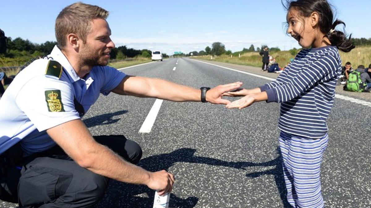 Un policía danés juega con una niña siria mientras el grupo con el que viaja cruza la carretera E45 dirección a Suecia.