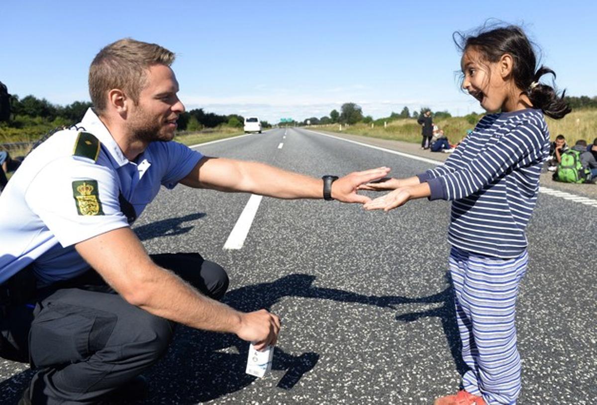 Un policia danès juga amb una nena siriana mentre el grup amb què viatja travessa la carretera E45 en direcció a Suècia.
