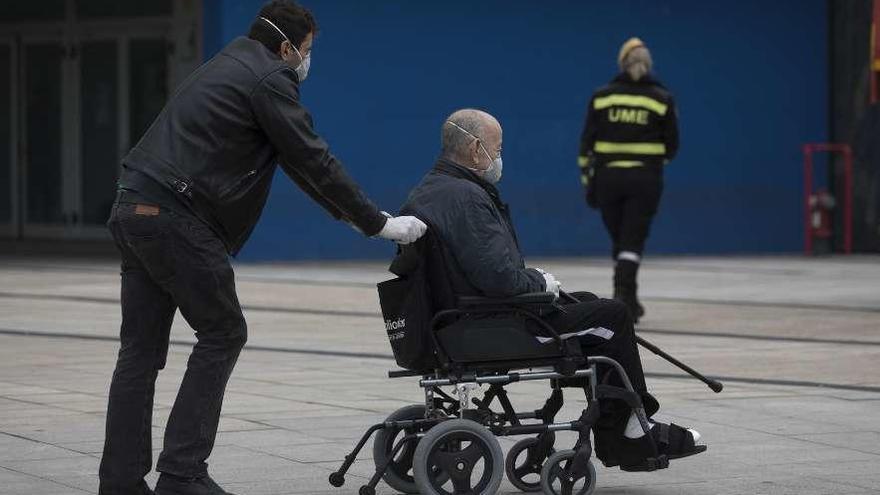 Un hombre lleva en una silla de ruedas a una persona mayor, a las puertas del HUCA.