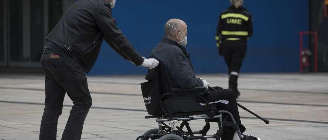 Un hombre lleva en una silla de ruedas a una persona mayor, a las puertas del HUCA.
