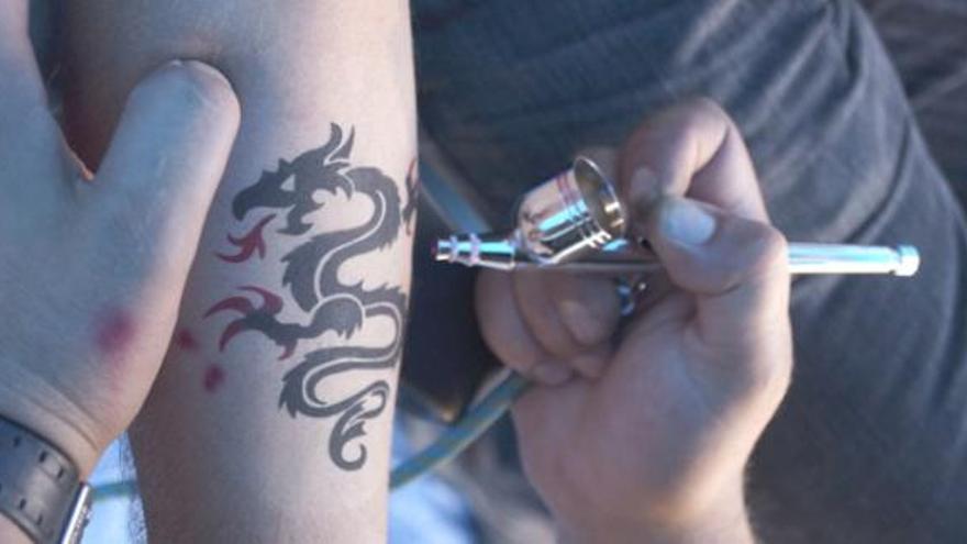 Un joven se realiza un tatuaje temporal de henna en el puesto de Peluquería Rober de la Concentración Motera &quot;La Peregrinación&quot;.