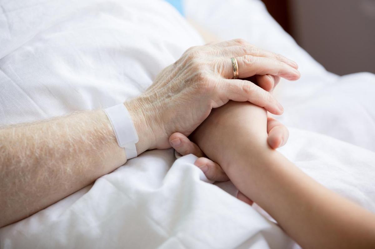 Primer plano del paciente, abuelo y niño tomados de la mano en la cama del hospital