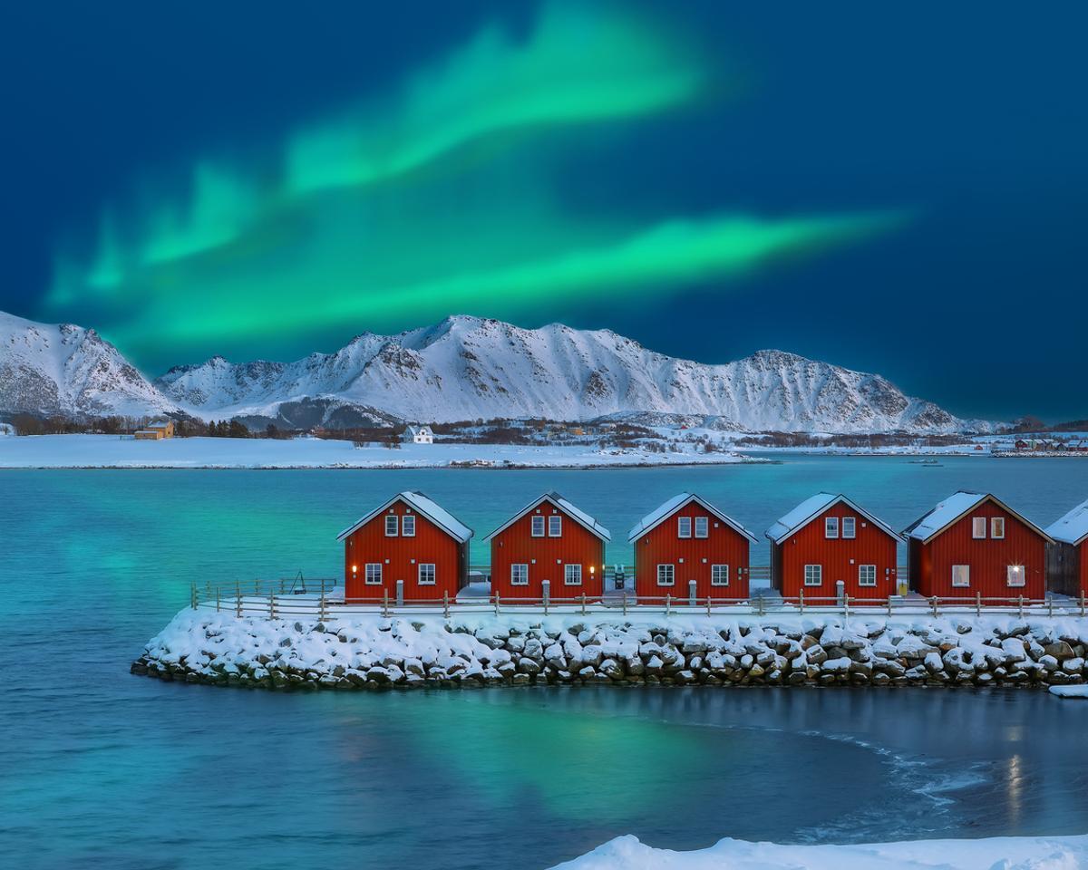 Increíble paisaje con casas tradicionales de madera roja en la orilla del fiordo Offersoystraumen con las auroras boreales bailando en el cieloisto