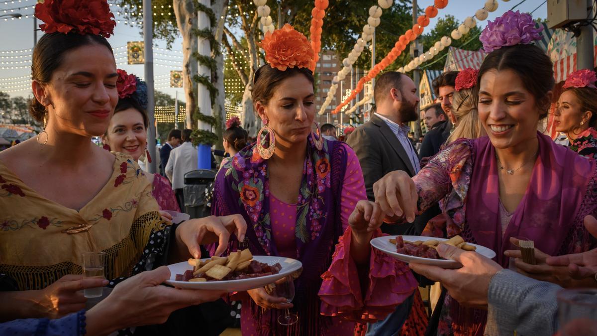 Varias mujeres vestidas de gitana toman chacinas en el Real de la Feria de Abril de Sevilla.